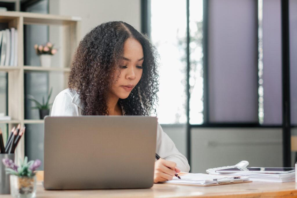 Intensely focused, a businesswoman works diligently on her laptop at a spacious desk in a modern, naturally lit office.