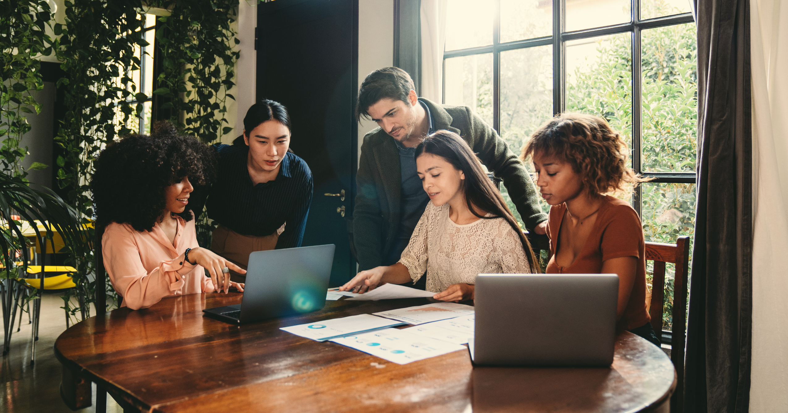 a group of people gathered around a table in an office setting looking at a laptop